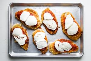 pan fried breaded chicken breast on a baking sheet topped with marinara and mozzarella
