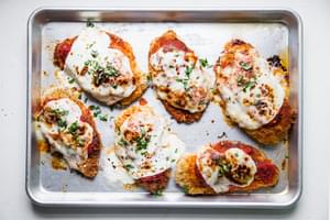 pan fried breaded chicken breast then baked topped with marinara and mozzarella and sprinkled with basil on a baking sheet