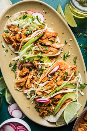 chicken Tinga tacos on a platter topped with avocado and radishes