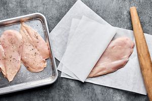 chicken being pounded between parchment paper then seasoned with salt and pepper
