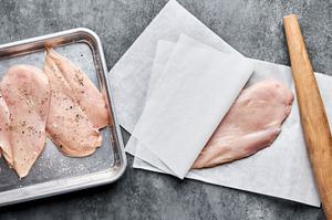 chicken being pounded between parchment paper then seasoned with salt and pepper