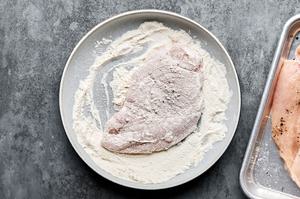 pounded chicken seasoned with salt and pepper being dredged in flour