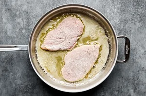flour dredged chicken being cooked in butter and olive oil in a skillet