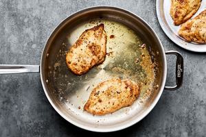 flour dredged chicken being cooked in butter and olive oil in a skillet