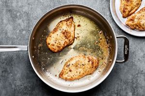 flour dredged chicken being cooked in butter and olive oil in a skillet