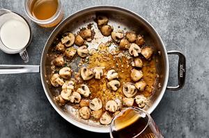 chicken stock and wine being added to a skillet with shallots, mushrooms, garlic and thyme