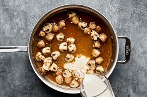 cream being added to a skillet with chicken stock, wine, shallots, mushrooms, garlic and thyme