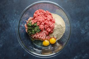 raw ground beef and ground pork in a bowl with chimichurri eggs and breadcrumbs