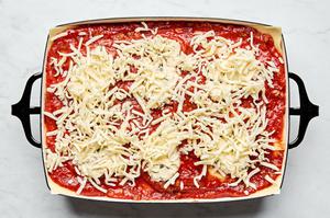 meat sauce, lasagna noodles and ricotta mixture being layered in a baking dish topped with mozzarella and Parmesan