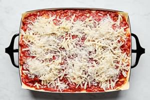 meat sauce, lasagna noodles and ricotta mixture being layered in a baking dish topped with mozzarella and Parmesan