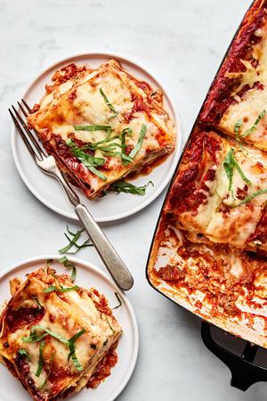 a pan of classic lasagna made with meat sauce, mozzarella, Parm, ricotta, and lasagna noodles being dished on to plates
