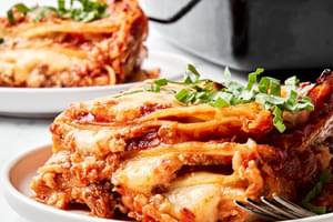a pan of classic lasagna made with meat sauce, mozzarella, Parm, ricotta, and  lasagna noodles being dished on to plates