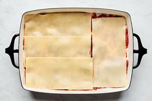 meat sauce, lasagna noodles and ricotta mixture being layered in a baking dish