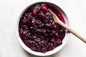 homemade cranberry sauce in a serving bowl with a wooden spoon made with orange juice, cinnamon, cloves and vanilla