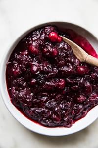 homemade cranberry sauce in a serving bowl with a wooden spoon made with orange juice, cinnamon, cloves and vanilla