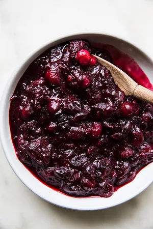 homemade cranberry sauce in a serving bowl with a wooden spoon made with orange juice, cinnamon, cloves and vanilla