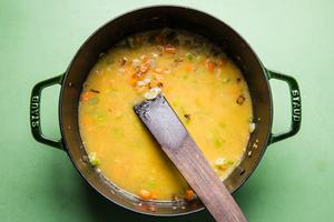 onions, carrots, celery, garlic butter, flour and chicken broth being stirred in a pot with a wooden spoon