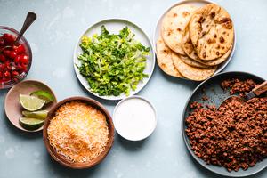 ground taco beef, fried tortillas, shredded lettuce, limes, salsa, Mexican cheese and sour cream