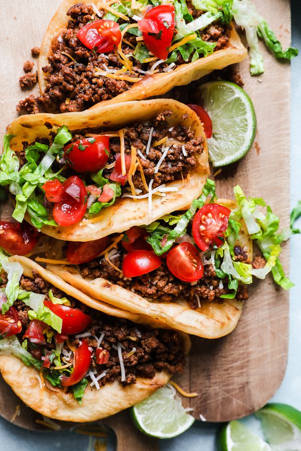 crispy beef tacos with cheese, shredded lettuce, tomatoes, and lime