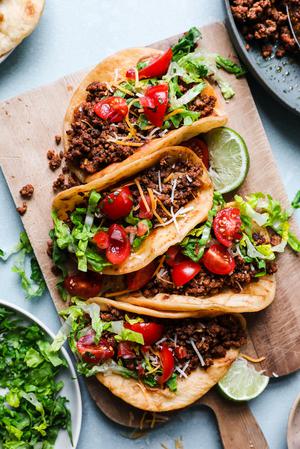 ground beef tacos with shredded lettuce, limes, salsa, Mexican cheese and sour cream