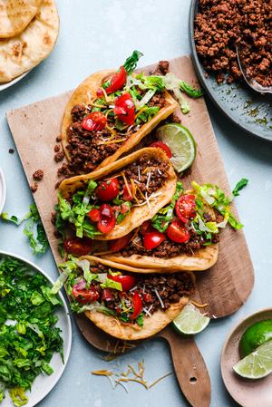 ground beef tacos with shredded lettuce, limes, salsa, Mexican cheese and sour cream