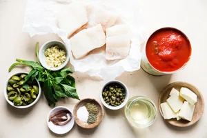 raw white fish on parchment, canned whole tomatoes, green olives, basil, garlic, anchovies, butter, white wine, cappers, salt