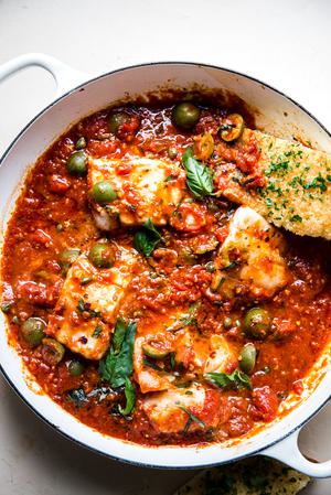 homemade white fish puttanesca in a baking dish with olives, capers and basil with garlic bread.