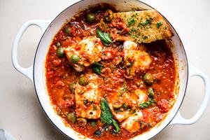homemade white fish puttanesca in a braising dish with garlic bread