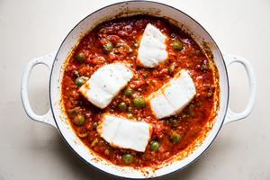 raw white fish in puttanesca sauce with butter, garlic, anchovies, white wine, spices, capers and olives in a braising dish