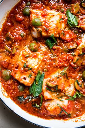 homemade white fish puttanesca in a baking dish with olives, capers and basil