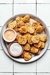 homemade fried pickles on a serving plate with bowls of ranch dressing and fry sauce for dipping