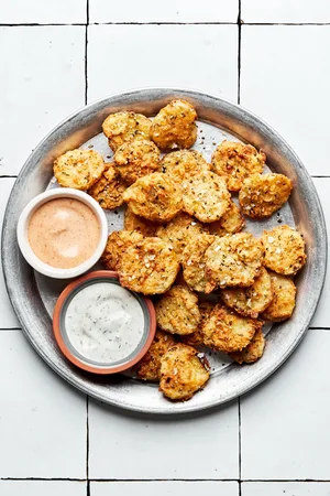 homemade fried pickles on a serving plate with bowls of ranch dressing and fry sauce for dipping