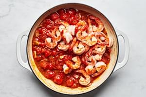 shrimp, tomatoes, garlic, oregano, thyme, garlic powder, sugar, salt and crushed red pepper flakes being cooked in a skillet