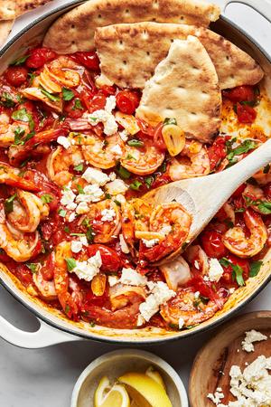Greek shrimp in a skillet topped with fresh parsley, lemon juice and feta served with pita bread