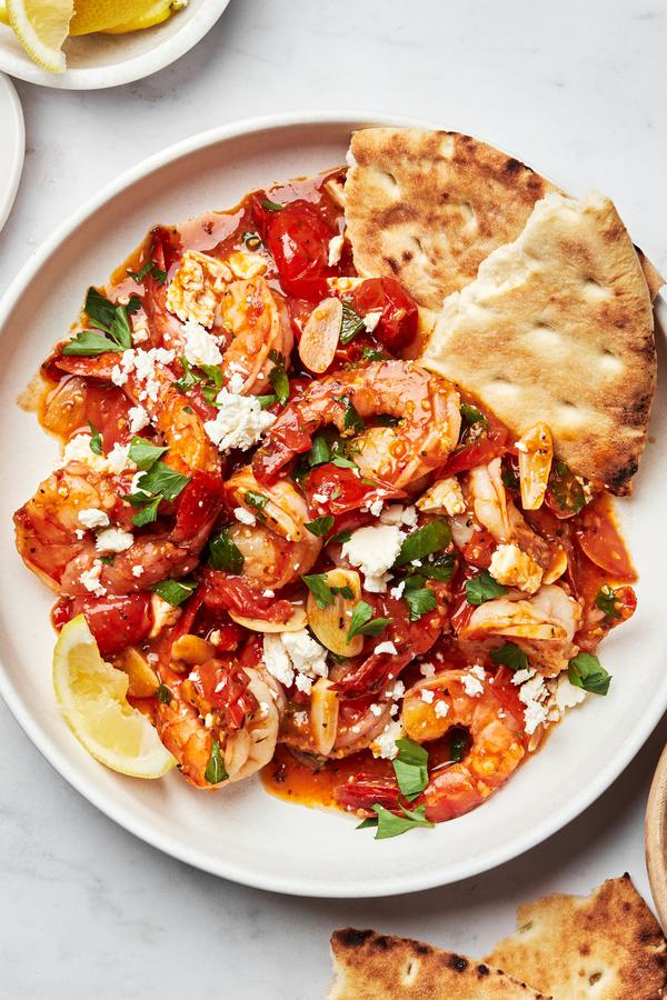 greek shrimp on a plate topped with parsley, lemon juice and feta served with pita bread