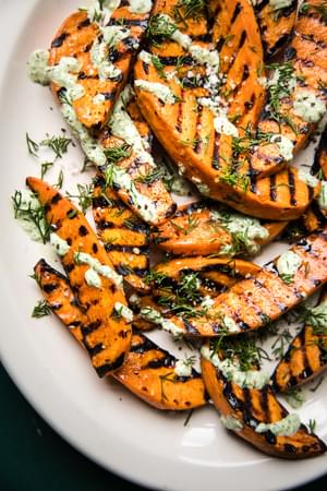 Grilled Sweet potatoes with olive oil and sea salt on a plate drizzled with a basil & dill yogurt sauce