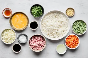 ingredients for ham fried rice laid out in bowls: eggs, carrots, onion, ham, rice, peas, green onions and soy sauce