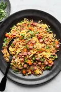 A bowl of ham fried rice, featuring fluffy rice mixed with diced ham, scrambled egg, peas & carrots, topped with green onions