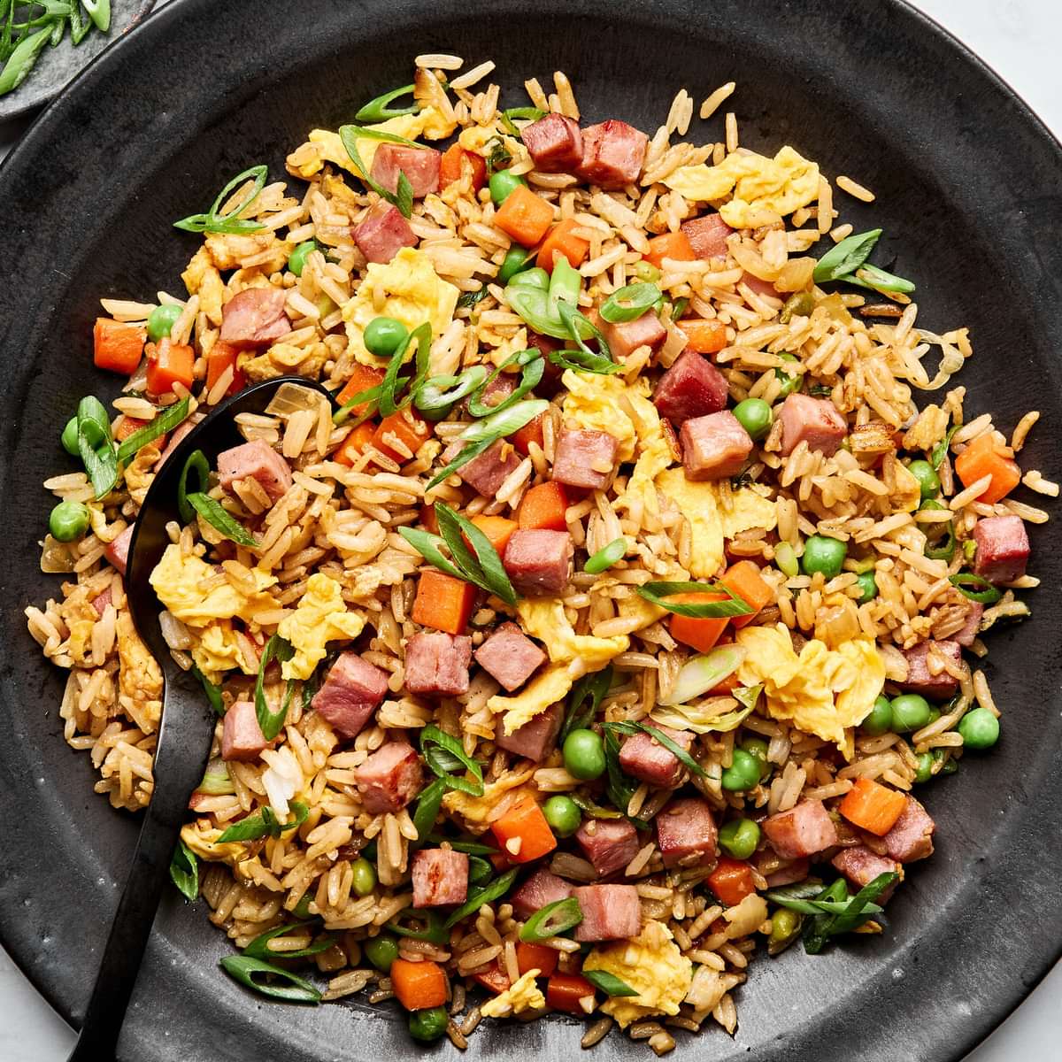 A bowl of ham fried rice, featuring fluffy rice mixed with diced ham, scrambled egg, peas & carrots, topped with green onions