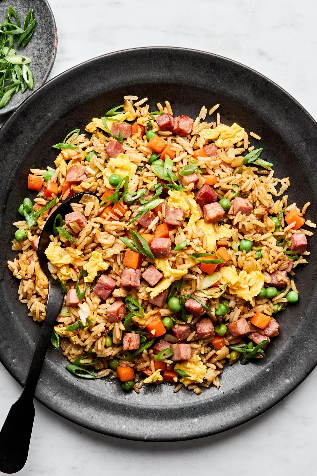 A bowl of ham fried rice, featuring fluffy rice mixed with diced ham, scrambled egg, peas & carrots, topped with green onions