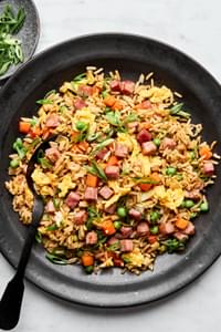 A bowl of ham fried rice, featuring fluffy rice mixed with diced ham, scrambled egg, peas & carrots, topped with green onions