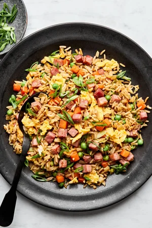 A bowl of ham fried rice, featuring fluffy rice mixed with diced ham, scrambled egg, peas & carrots, topped with green onions
