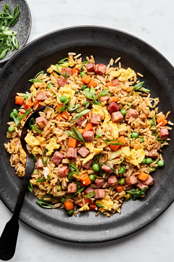 A bowl of ham fried rice, featuring fluffy rice mixed with diced ham, scrambled egg, peas & carrots, topped with green onions
