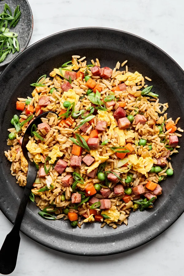 A bowl of ham fried rice, featuring fluffy rice mixed with diced ham, scrambled egg, peas & carrots, topped with green onions