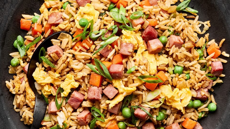 A bowl of ham fried rice, featuring fluffy rice mixed with diced ham, scrambled egg, peas & carrots, topped with green onions