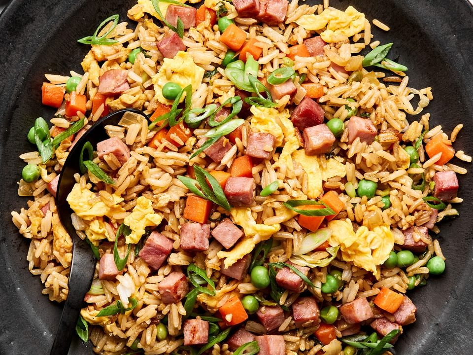A bowl of ham fried rice, featuring fluffy rice mixed with diced ham, scrambled egg, peas & carrots, topped with green onions