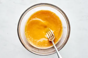 eggs, coconut aminos, sesame oil and salt being whisked by a fork in a glass bowl