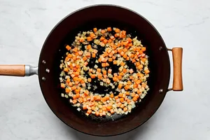carrots, onion and garlic being cooked in vegetable oil in a wok