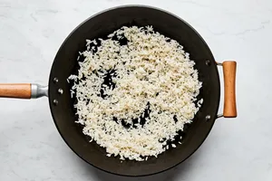rice being fried in sesame oil and vegetable oil in a wok