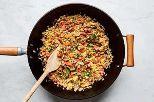 Ham fried rice sizzling in a hot wok, with diced ham, scrambled egg, peas, carrots, and rice being stir-fried together